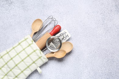Photo of Different kitchen utensils in oven mitten on light table, top view. Space for text