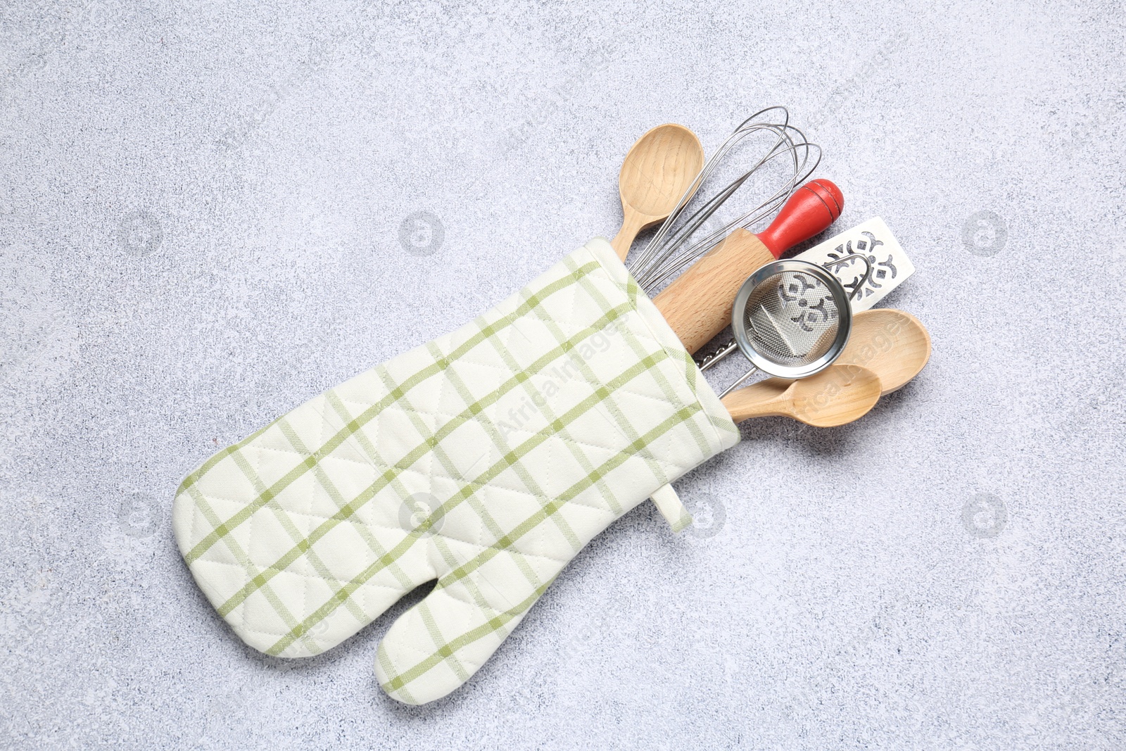 Different kitchen utensils in oven mitten on light table, top view Photo of Different kitchen utensils in oven mitten on light table, top view