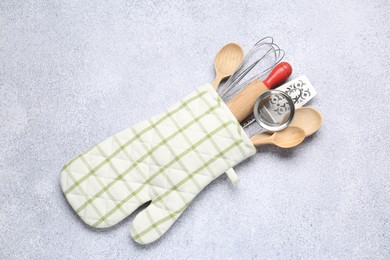 Photo of Different kitchen utensils in oven mitten on light table, top view