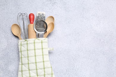 Photo of Different kitchen utensils in oven mitten on light table, top view. Space for text