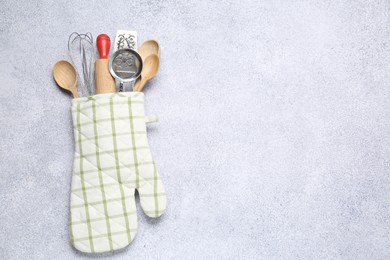 Photo of Different kitchen utensils in oven mitten on light table, top view. Space for text