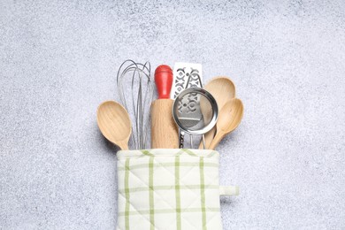 Photo of Different kitchen utensils in oven mitten on light table, top view