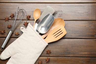 Photo of Different kitchen utensils in oven mitten and anise stars on wooden table, flat lay