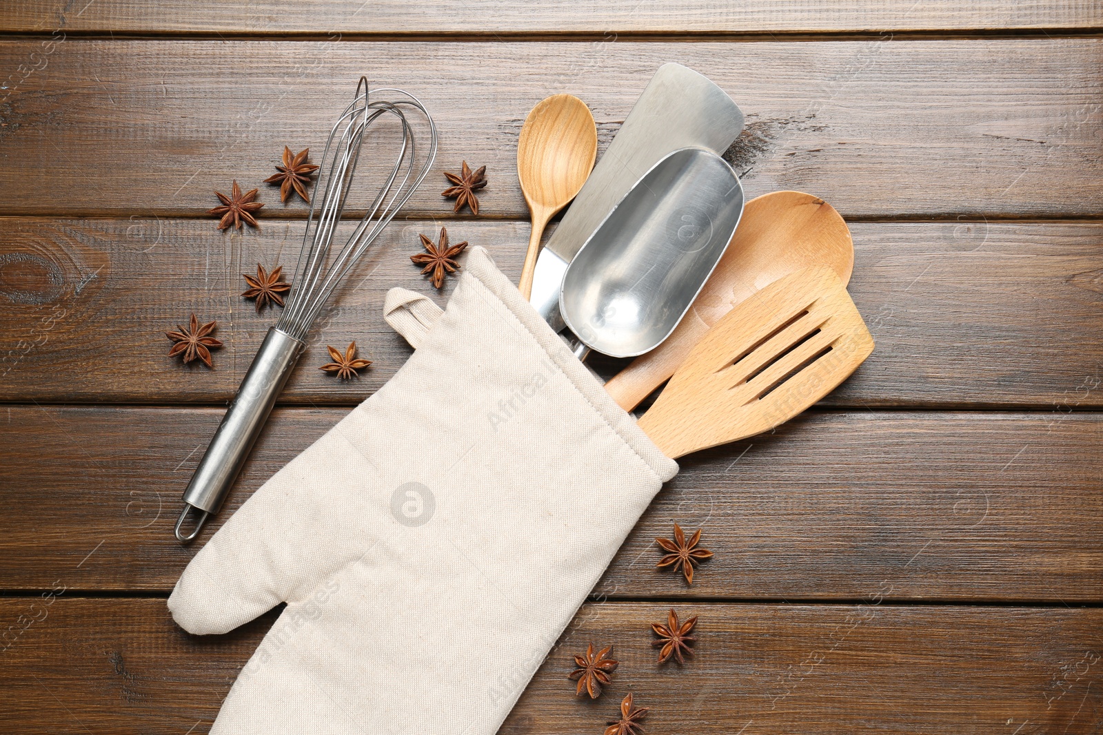 Different kitchen utensils in oven mitten and anise stars on wooden table, flat lay Photo of Different kitchen utensils in oven mitten and anise stars on wooden table, flat lay