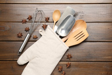 Photo of Different kitchen utensils in oven mitten and anise stars on wooden table, flat lay
