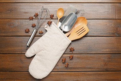 Photo of Different kitchen utensils in oven mitten and anise stars on wooden table, flat lay