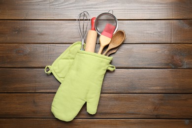 Photo of Different kitchen utensils in oven mitten on wooden table, top view