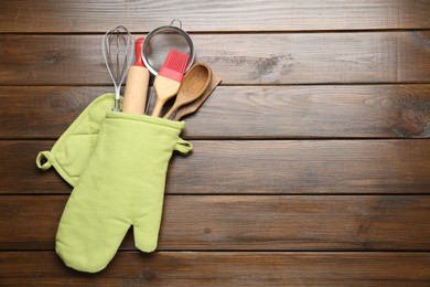 Photo of Different kitchen utensils in oven mitten on wooden table, top view. Space for text