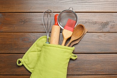 Photo of Different kitchen utensils in oven mitten on wooden table, top view