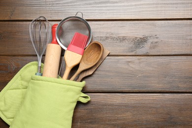 Photo of Different kitchen utensils in oven mitten on wooden table, top view. Space for text