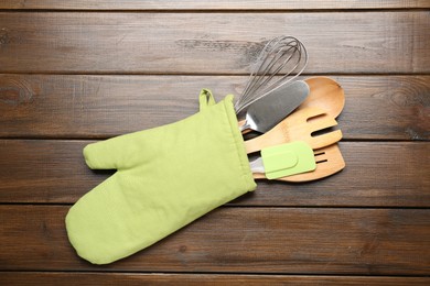 Photo of Different kitchen utensils in oven mitten on wooden table, top view