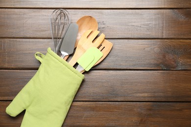 Photo of Different kitchen utensils in oven mitten on wooden table, top view. Space for text
