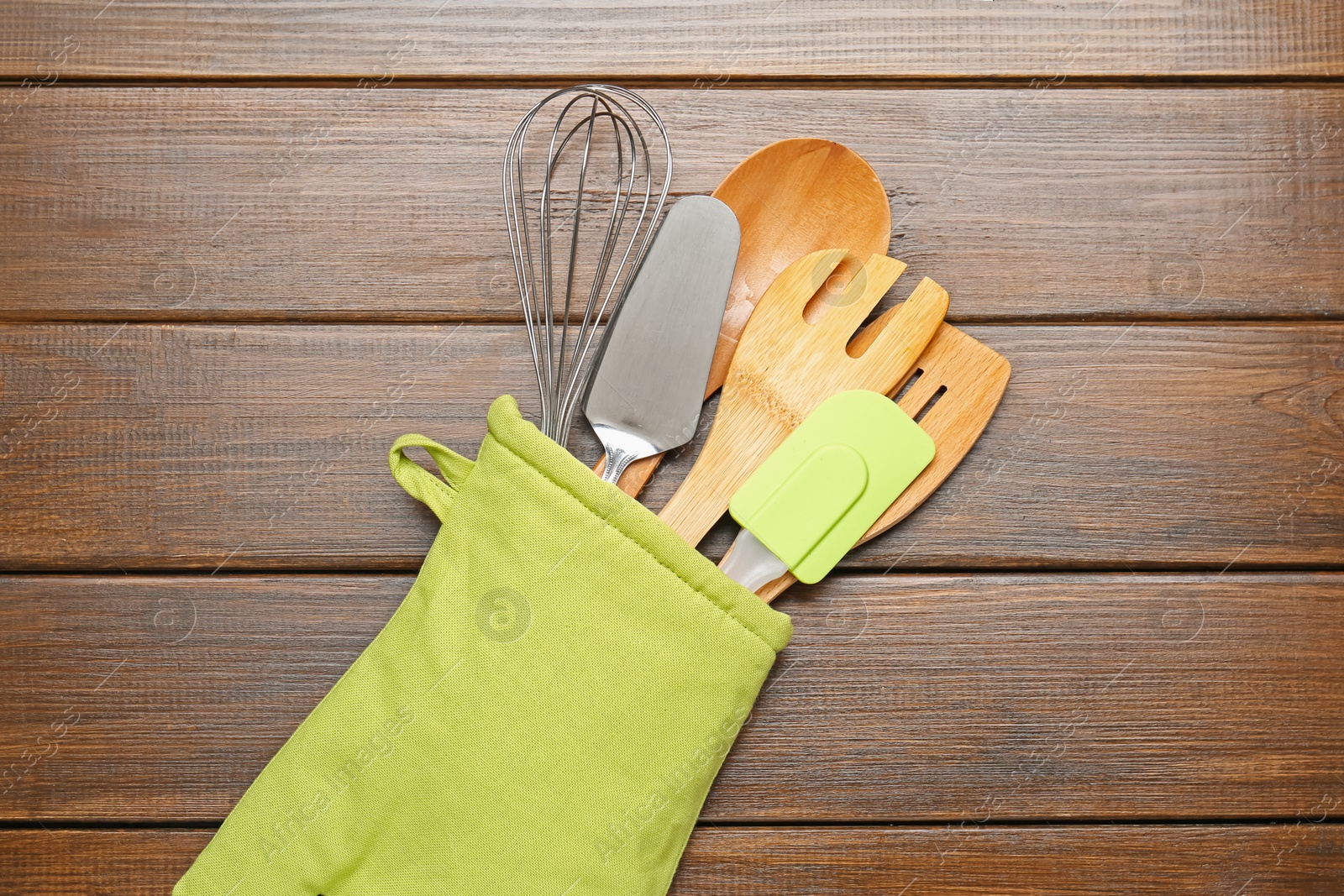 Different kitchen utensils in oven mitten on wooden table, top view Photo of Different kitchen utensils in oven mitten on wooden table, top view