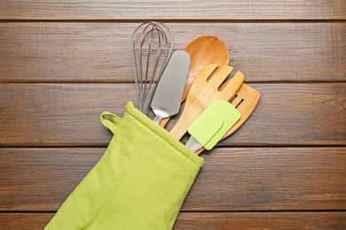 Photo of Different kitchen utensils in oven mitten on wooden table, top view