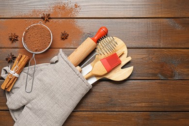 Photo of Different kitchen utensils in oven mitten, cocoa powder, cinnamon and anise stars on wooden table, flat lay