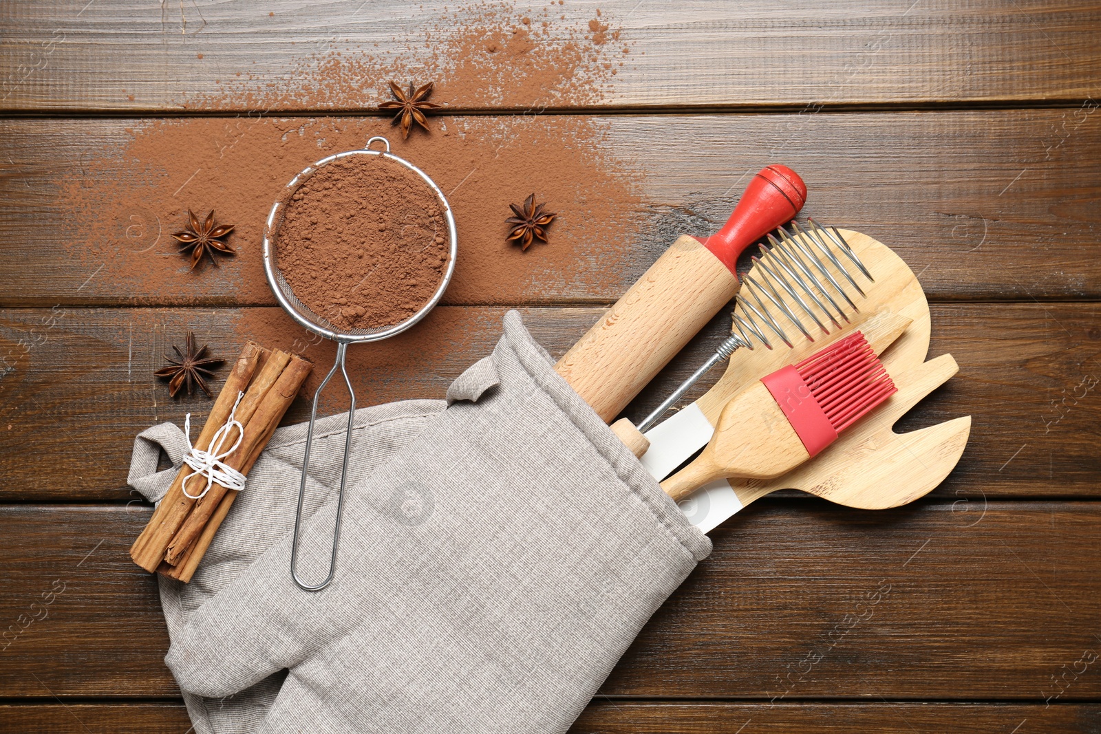 Different kitchen utensils in oven mitten, cocoa powder, cinnamon and anise stars on wooden table, flat lay Photo of Different kitchen utensils in oven mitten, cocoa powder, cinnamon and anise stars on wooden table, flat lay