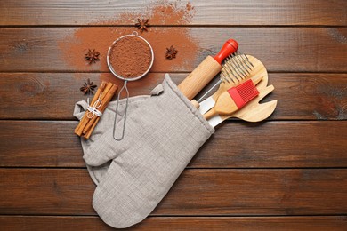 Photo of Different kitchen utensils in oven mitten, cocoa powder, cinnamon and anise stars on wooden table, flat lay