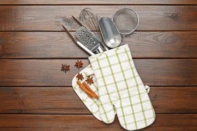 Photo of Different kitchen utensils in oven mitten, cinnamon and anise stars on wooden table, flat lay