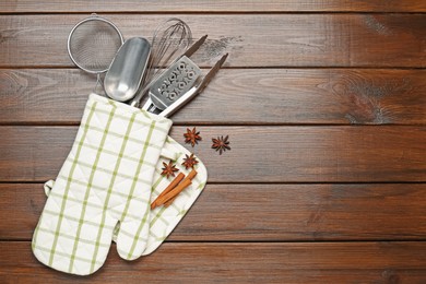 Photo of Different kitchen utensils in oven mitten, cinnamon and anise stars on wooden table, flat lay. Space for text