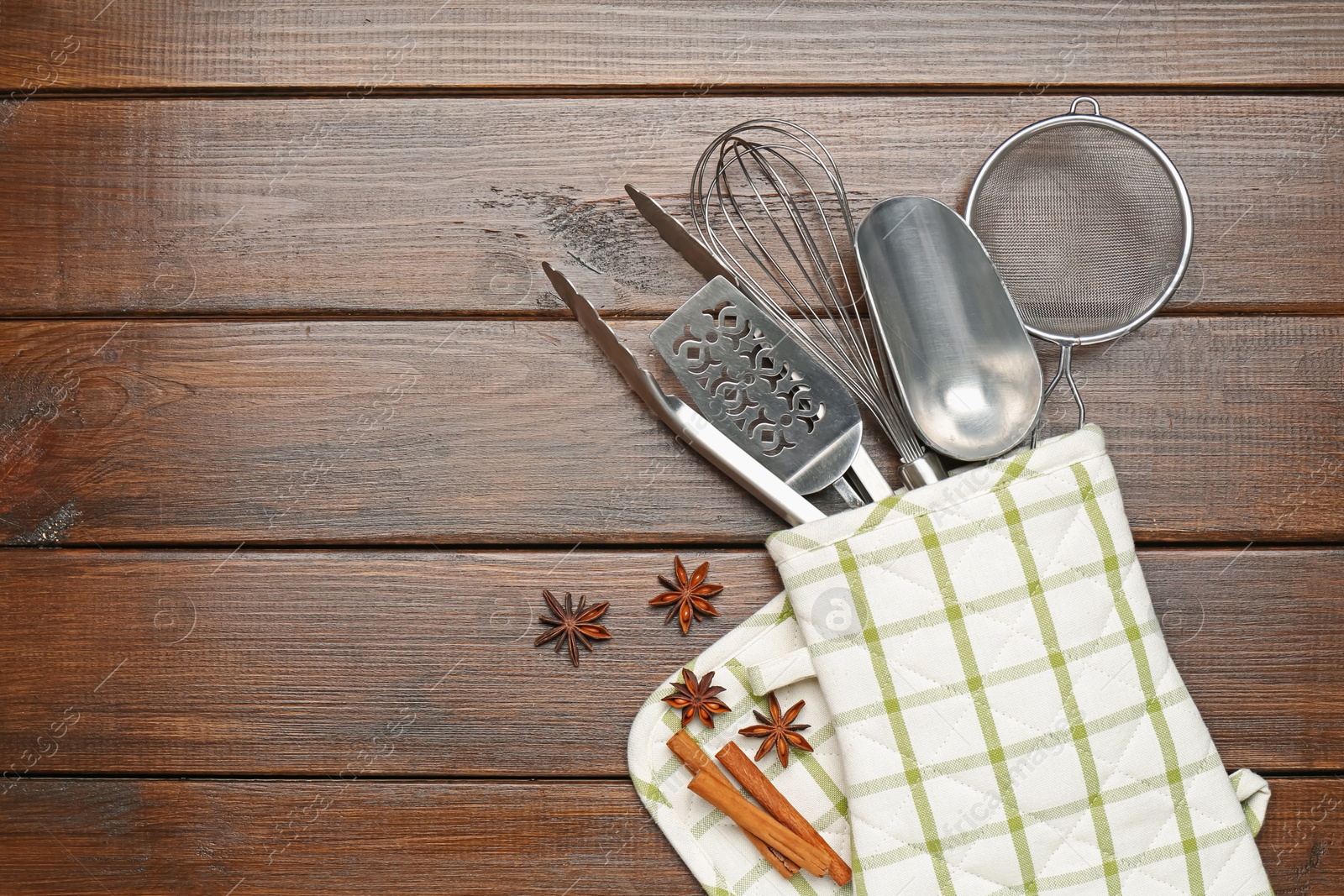 Different kitchen utensils in oven mitten, cinnamon and anise stars on wooden table, flat lay. Space for text Photo of Different kitchen utensils in oven mitten, cinnamon and anise stars on wooden table, flat lay. Space for text