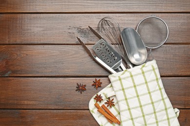Photo of Different kitchen utensils in oven mitten, cinnamon and anise stars on wooden table, flat lay. Space for text