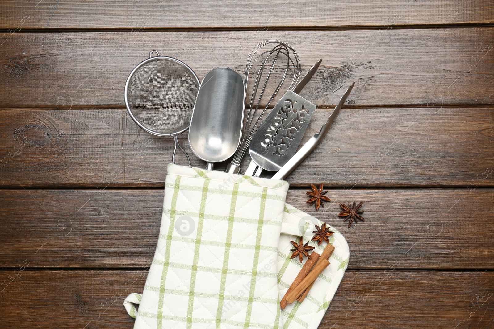 Different kitchen utensils in oven mitten, cinnamon and anise stars on wooden table, flat lay Photo of Different kitchen utensils in oven mitten, cinnamon and anise stars on wooden table, flat lay