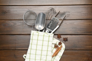 Photo of Different kitchen utensils in oven mitten, cinnamon and anise stars on wooden table, flat lay