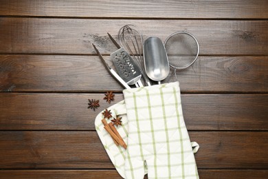 Photo of Different kitchen utensils in oven mitten, cinnamon and anise stars on wooden table, flat lay