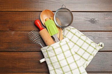 Photo of Different kitchen utensils in oven mitten on wooden table, top view