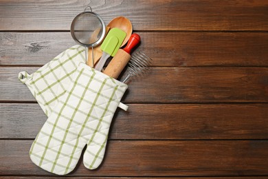 Photo of Different kitchen utensils in oven mitten on wooden table, top view. Space for text