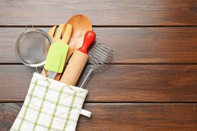 Photo of Different kitchen utensils in oven mitten on wooden table, top view. Space for text