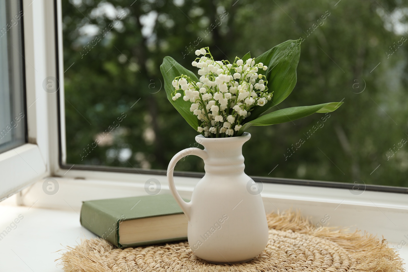 Bouquet of lily-of-the-valley flowers in vase and book on windowsill indoors Photo of Bouquet of lily-of-the-valley flowers in vase and book on windowsill indoors