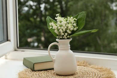 Photo of Bouquet of lily-of-the-valley flowers in vase and book on windowsill indoors