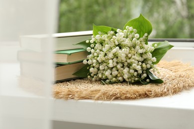 Photo of Bouquet of lily-of-the-valley flowers and books on windowsill indoors