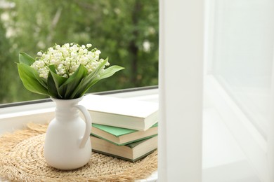 Photo of Bouquet of lily-of-the-valley flowers in vase and books on windowsill indoors