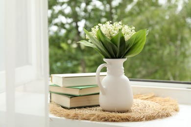 Photo of Bouquet of lily-of-the-valley flowers in vase and books on windowsill indoors