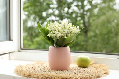 Photo of Bouquet of lily-of-the-valley flowers in vase and apple on windowsill indoors