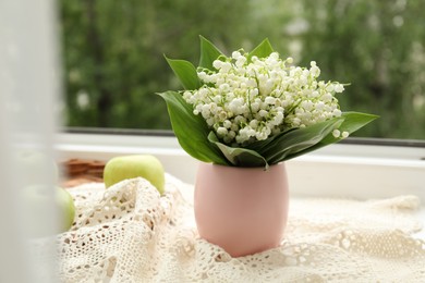 Photo of Bouquet of lily-of-the-valley flowers in vase and apple on windowsill indoors