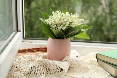 Photo of Bouquet of lily-of-the-valley flowers in vase and books on windowsill indoors