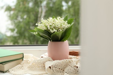 Photo of Bouquet of lily-of-the-valley flowers in vase and books on windowsill indoors