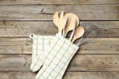 Photo of Different kitchen utensils in oven mitten on wooden table, top view