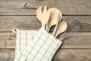Photo of Different kitchen utensils in oven mitten on wooden table, top view