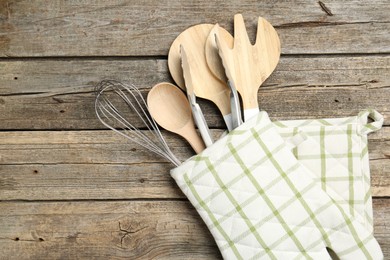 Photo of Different kitchen utensils in oven mitten on wooden table, top view. Space for text