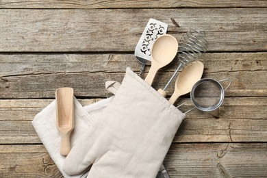 Photo of Different kitchen utensils in oven mitten on wooden table, top view