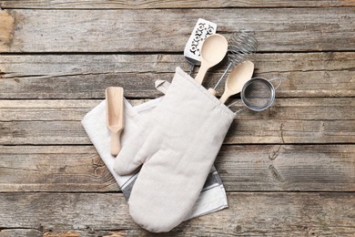 Photo of Different kitchen utensils in oven mitten on wooden table, top view
