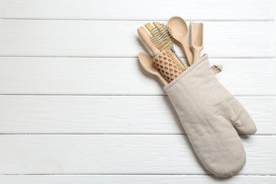 Photo of Different kitchen utensils in oven mitten on white wooden table, top view. Space for text