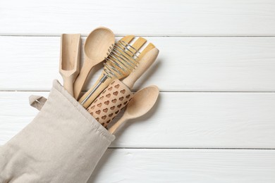 Photo of Different kitchen utensils in oven mitten on white wooden table, top view. Space for text