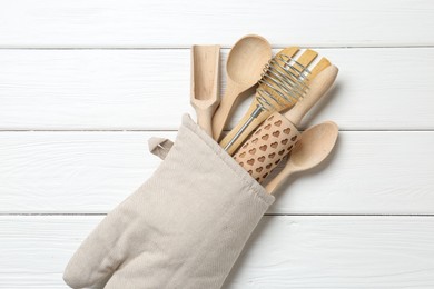 Photo of Different kitchen utensils in oven mitten on white wooden table, top view