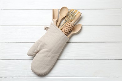 Photo of Different kitchen utensils in oven mitten on white wooden table, top view