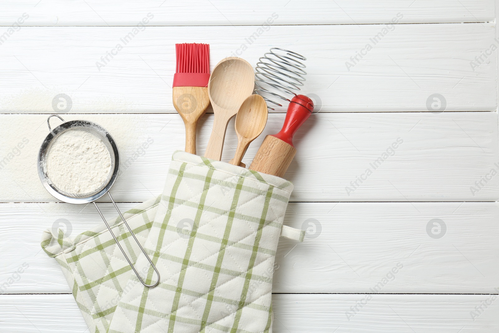 Different kitchen utensils in oven mitten and flour on white wooden table, flat lay. Space for text Photo of Different kitchen utensils in oven mitten and flour on white wooden table, flat lay. Space for text
